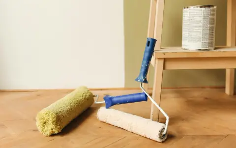 Färgburk och roller på trägolv, redo att måla på tapet.