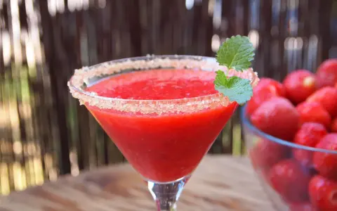 Orzeźwiający strawberry daiquiri z cukrowym rantem i listkiem mięty, obok miska pełna świeżych truskawek.