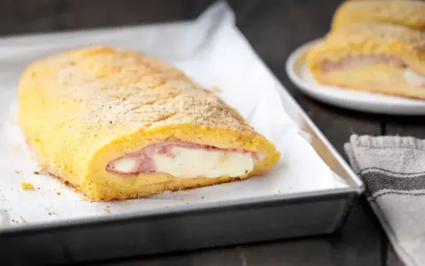 Rotolo dorato di polpettone di patate ripieno di prosciutto e formaggio filante, pronto per essere gustato.
