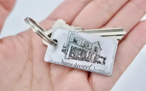Un llavero hogar con la imagen de una casa y la frase "home sweet home" descansa en una mano.