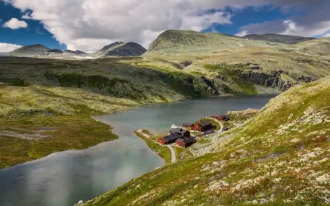 En vacker vy över en sjö med röda stugor vid en fjällsluttning, perfekt för en triangeltur i Norge.