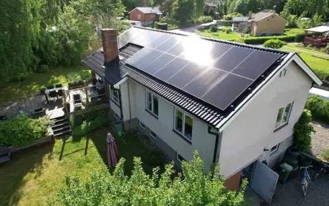 Ett hus med solpaneler på taket, redo att fånga solens energi. En grönskande trädgård och en altan inbjuder till avkoppling.