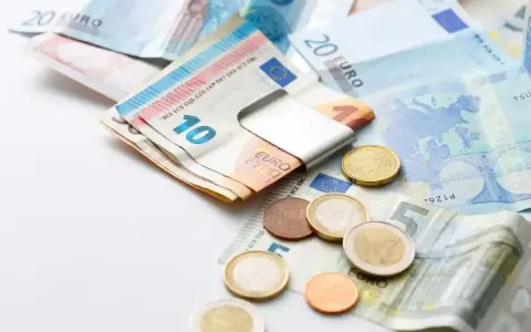 Euro banknoty i monety, czyli waluta w Grecji. Widać banknot 10 euro w metalowym klipsie, a obok monety i banknoty 5, 20 euro.