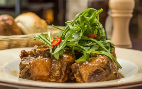 Delicioso rabo de toro en salsa, coronado con rúcula fresca y rodajas de chile. Una receta que conquista paladares.