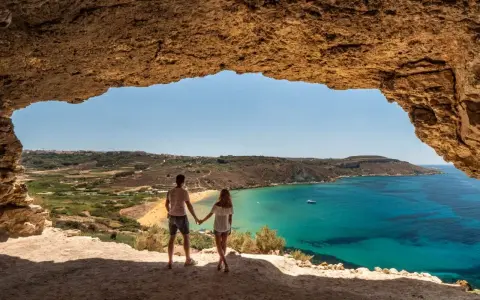 Para w jaskini podziwia widok na turkusowe morze i plażę. Malta pogoda wrzesień idealna na wakacje.