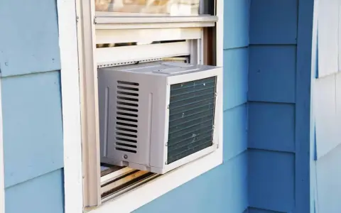 Climatisation réversible sans groupe extérieur installée dans une fenêtre. L'unité blanche est visible sur un mur bleu.