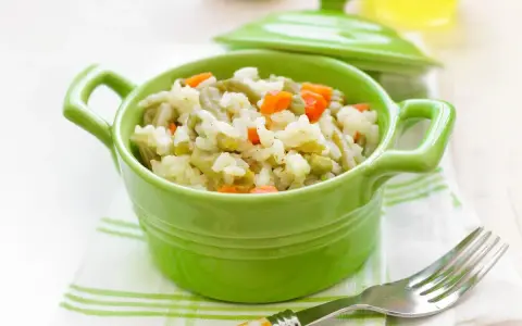 Un tazón verde vibrante lleno de arroz con verduras para bebé, con zanahorias y guisantes.