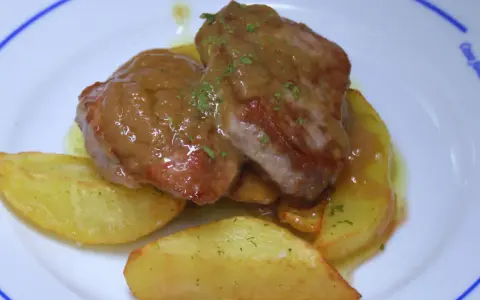 Solomillo jugoso con salsa de whisky sobre patatas gajo en un plato blanco.