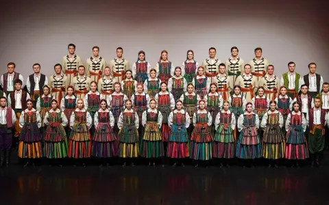 Zespół w barwnych strojach ludowych, prezentujący mazowieckie piosenki ludowe.