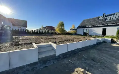 Nowe schody i betonowy murek to co zamiast muru oporowego, otaczają plac budowy domu z panelami słonecznymi.