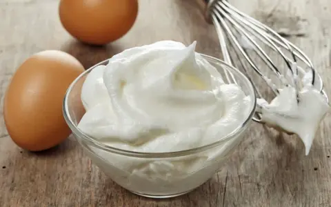Zwei Eier und ein Schneebesen neben einer Schüssel mit luftigem Eischnee, der nicht fest wird.