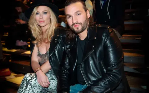 Steve Angello fru, Isabella, med sin blonda frisyr och hatt, sitter bredvid honom. Båda bär svarta läderjackor.