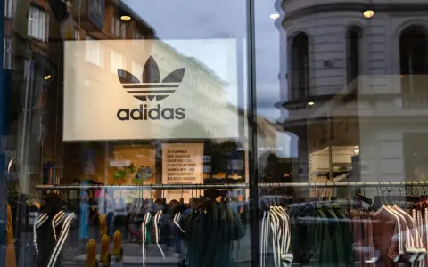 Witryna sklepu z logo adidas, marki pochodzącej z Niemiec. Wieszaki z ubraniami, w tym kurtki i bluzy z charakterystycznymi trzema paskami.
