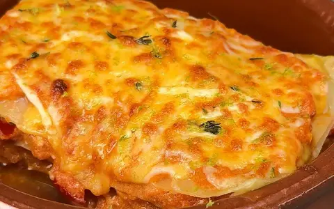 Deliciosa lasaña de atún gratinada con queso dorado y hierbas frescas, servida en una cazuela de barro.