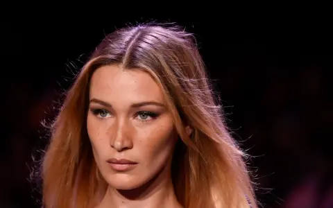 Primo piano di una modella con capelli biondi mossi e occhi verdi penetranti. La sua espressione è enigmatica, quasi a chiedersi chi è la donna più bella del mondo.