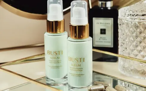 Dwa flakoniki serum ujędrniającego do biustu Busti, kapsułki i eleganckie flakony w tle.