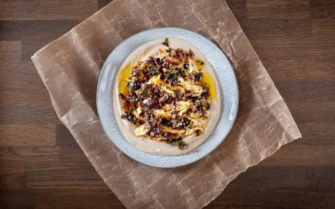 En krämig aubergine i ugn serveras på en bädd av hummus, toppad med en smakrik blandning av oliver, kapris och örter.