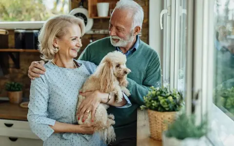 Uśmiechnięta para seniorów trzyma pudla. Idealny pies dla seniora, który wnosi radość i towarzystwo.