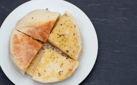 Pokrojone na ćwiartki bolo do caco, posypane ziołami, na białym talerzu.