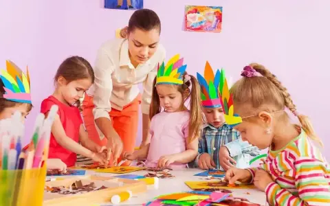 Nauczycielka pomaga dzieciom w tworzeniu pióropuszy. Jedno z dzieci, 4-latek, nie chce się bawić z dziećmi, ale skupia się na pracy.