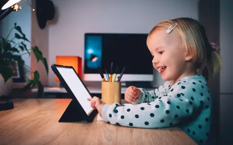 Uśmiechnięta dziewczynka ogląda ulubionych youtuberów dla dzieci na tablecie.