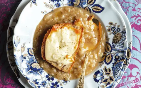 Piatto di zuppa di cipolle fumante, con crostino di pane e formaggio fuso, servita su un elegante piatto decorato.