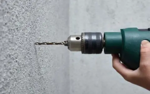 Taladrando hormigón con un taladro. La broca se adentra en la pared texturizada.