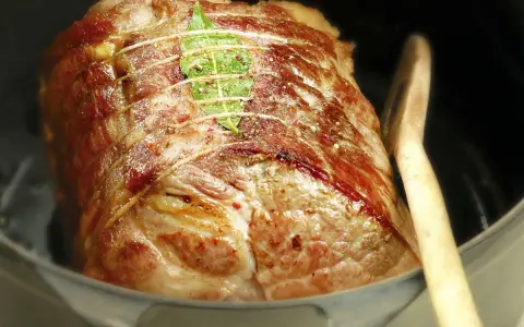 Un rôti de porc cocotte, doré et savoureux, est prêt à cuire dans sa cocotte avec une feuille de laurier et une cuillère en bois.