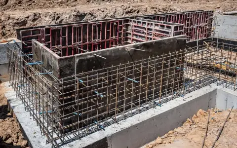 Siatka zbrojeniowa otacza betonowe szalunki, tworząc solidne zbrojenie ściany fundamentowej.