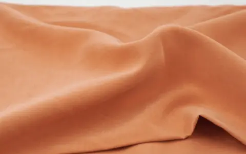 Miękka, pomarańczowa tkanina. Zastanawiasz się, **tencel co to**? To ekologiczny materiał o jedwabistym chwycie, idealny na letnie ubrania.