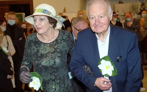 Ewa Dałkowska z synem Ksawerym, elegancko ubrani, z kwiatami w dłoniach, podczas uroczystości.