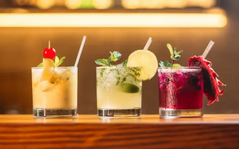 Trzy kolorowe drinki na barze: żółty z wiśnią, zielony z limonką i miętą, oraz fioletowy z pitają. Idealne do letnich wieczorów, a może i z **kazbek peak brandy z czym pić**?