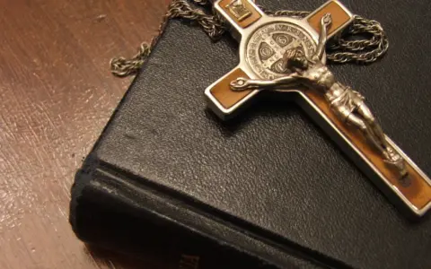 Krzyż z Jezusem i łańcuszek na czarnej księdze, symbol wiary i nadziei, narzędzia, które mógłby mieć przy sobie egzorcysta.