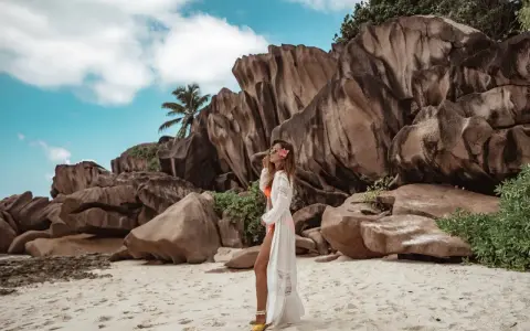 Kobieta w białej narzutce na plaży Anse Source d'Argent, Seszele. Co zobaczyć? Monumentalne granitowe skały i turkusowe niebo.