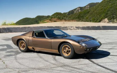 Ein brauner Lamborghini Miura S steht auf einer asphaltierten Straße mit Bergkulisse.