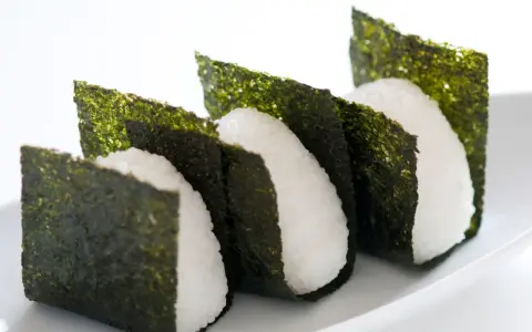 Trzy ryżowe onigiri owinięte w arkusze nori. Prosty sposób, jak przygotować nori do sushi, by nadać mu chrupkość i smak.
