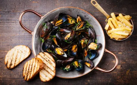 Moules marinières, une spécialité culinaire normande, servies dans une marmite en cuivre avec des frites et du pain grillé.