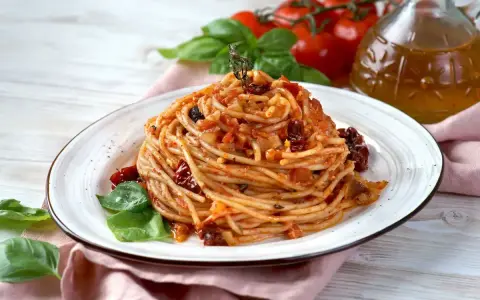 Un piatto di spaghetti conditi con un sugo rosso ricco di pomodori secchi, basilico fresco e un filo d'olio d'oliva.