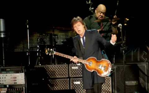Paul McCartney na jednym ze swoich koncertów, grając na gitarze basowej. W tle perkusista.