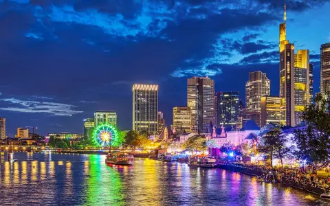 Frankfurt Mainufer bei Nacht: Lichtermeer, beleuchtetes Riesenrad und Skyline spiegeln sich im Wasser.