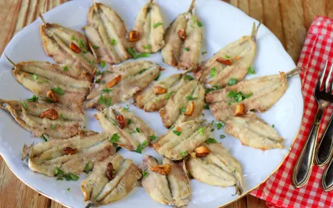 Un plato blanco con boquerones fritos, dorados y crujientes, espolvoreados con perejil fresco y trocitos de ajo.