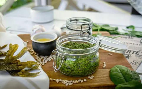 Frisches Pesto aus essbaren Algen der Nordsee, daneben Sonnenblumenkerne, Knoblauch und ein kleines Schälchen mit Öl.