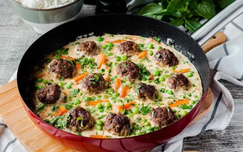 Herzhafte Fleischbällchen in cremiger Sauce mit Erbsen und Karotten, ein köstliches Wikingertopf Rezept, serviert in einer roten Pfanne.