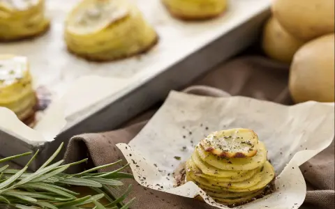 Tourte de pommes de terre fines et dorées, assaisonnée d'herbes, sur du papier sulfurisé.