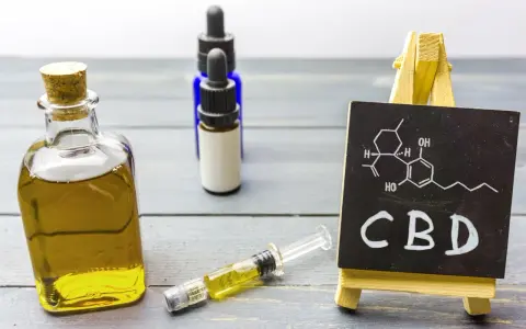 Butelka z olejkiem, strzykawka i tabliczka z napisem CBD. Zastanawiasz się, olejek CBD na co?