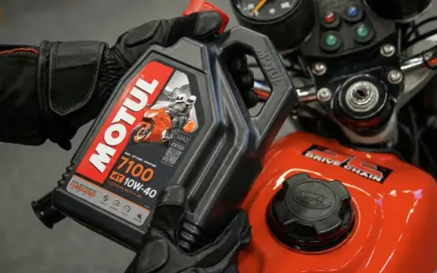 Ręce w rękawiczkach trzymają olej Motul 7100 10W-40. Pytanie: co ile wymieniać olej w motocyklu?