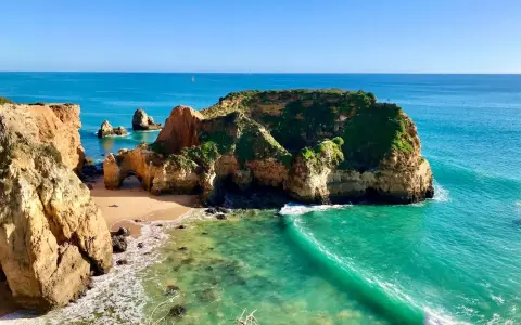 Traumhafte Felsformationen und türkisfarbenes Wasser am Praia de Alvor. Eine kleine Bucht mit Sand und grünen Klippen.
