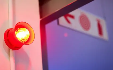 Czerwony alarm przeciwpożarowy miga, przypominając o tym, co to dysocjacja. Znak ewakuacyjny w tle.