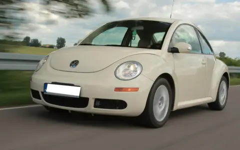 Jasny Volkswagen Beetle w ruchu na drodze, z rozmytym tłem.