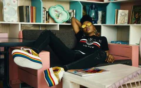 Une jeune femme aux lunettes rondes dorées se détend sur un canapé, ses chaussures arc-en-ciel colorées bien en évidence. Elle incarne le parfait "chill traduction".